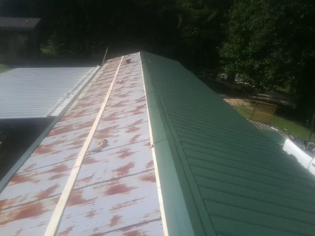Old rusted panels beside newly installed green metal roofing — Wind Damage Roof Repair by Roofing Brothers in Orange Springs