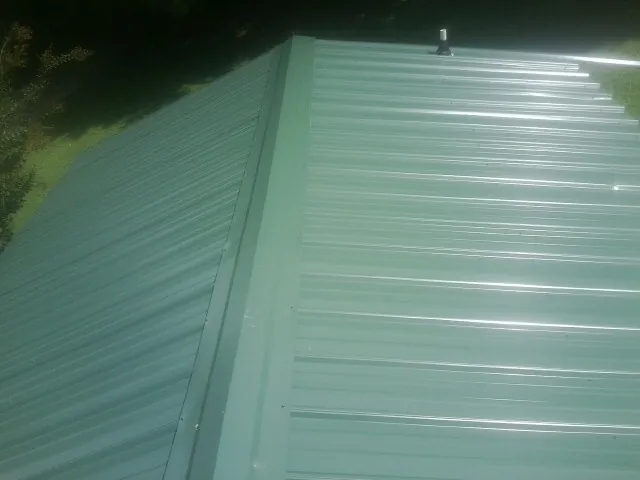 New green metal panels meeting at the ridge of a roof — Flat Roof Repair work by our crew in Orange Springs
