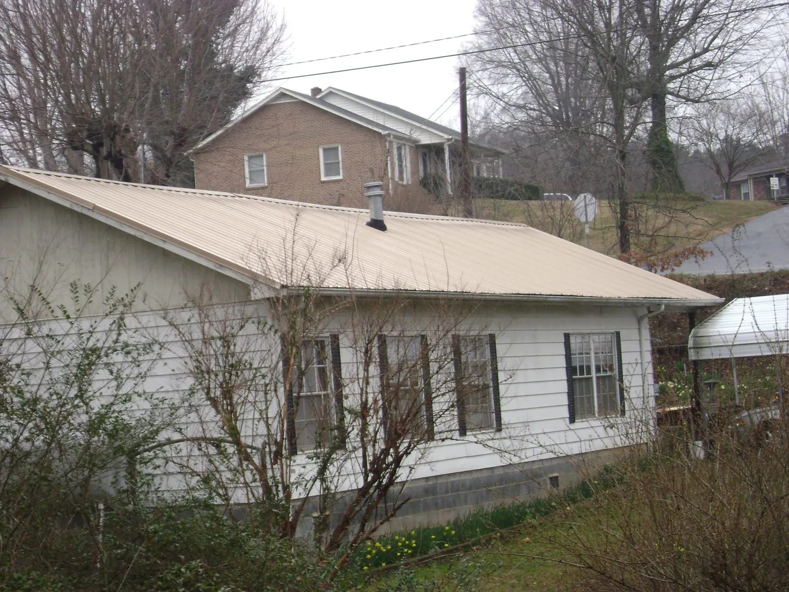 Tan metal roof on a white sided house set into a hillside — Commercial Roofing by Roofing Brothers in Orange Springs