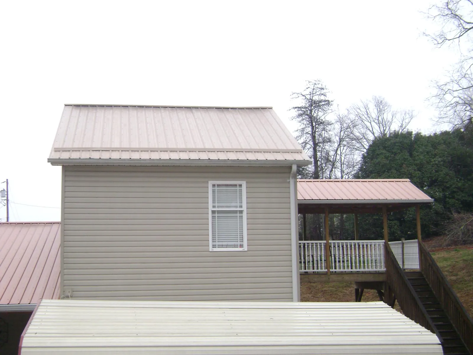 Tan metal roofs on a two story addition and attached porch, from a Roof Replacement job in Orange Springs